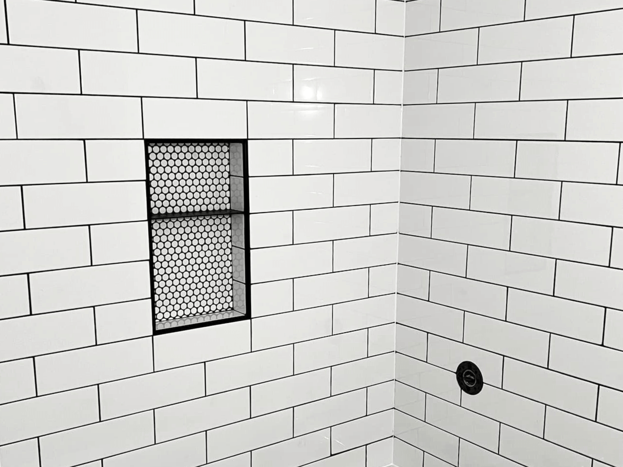 White subway tile with black grout featuring a Schluter System shelf. 